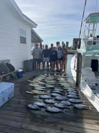 A group of anglers proudly displaying their catch of various fish on the dock after a successful fishing trip.