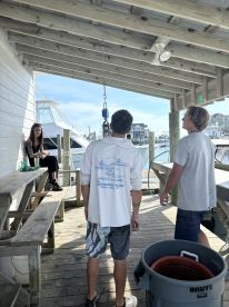 A group of individuals gathered at a dock, with a boat in the background, discussing their fishing experience.