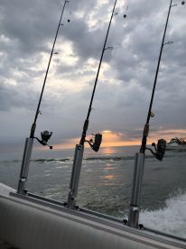 Fishing rods are set up on the side of a boat, with a beautiful sunset reflecting on the water, creating a serene fishing atmosphere.