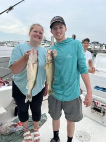 Two anglers proudly displaying their catch of Walleye on a fishing charter, with boats visible in the background.
