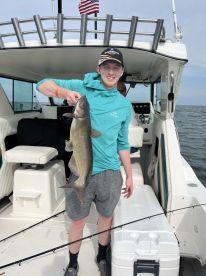 A young angler proudly displaying a large Catfish aboard a fishing boat, showcasing a successful day on the water.