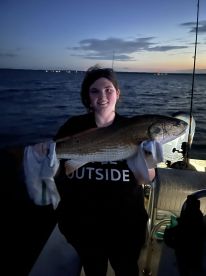 A young angler proudly displaying a large fish at sunset while fishing on a boat.
