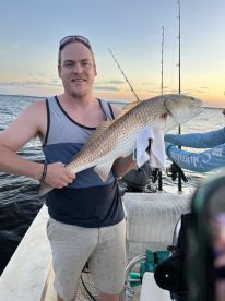 Angler proudly displaying a large Redfish while fishing on a boat during sunset.