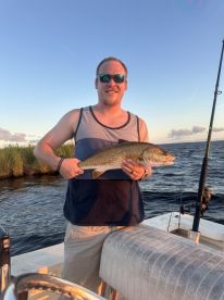 An angler proudly displaying a large Redfish while fishing on a boat during sunset.
