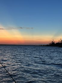 A serene sunset over the water, showcasing vibrant colors reflecting on the waves, ideal for a peaceful fishing experience.