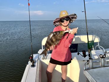 A young angler proudly displaying a Black Drum caught while fishing on a boat in calm waters.