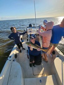A group of anglers enjoying a day on the water, with one proudly displaying a caught Redfish while aboard a center console boat.