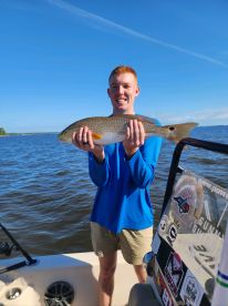 A young angler proudly displaying a Redfish while fishing on a sunny day.
