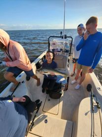 A group of anglers enjoying a successful day on the water, with a young woman proudly displaying a large striped bass aboard a fishing boat.