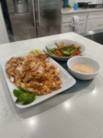 Plated grilled fish fillets served with lime wedges and a side of sautéed peppers, showcasing a delicious seafood meal.