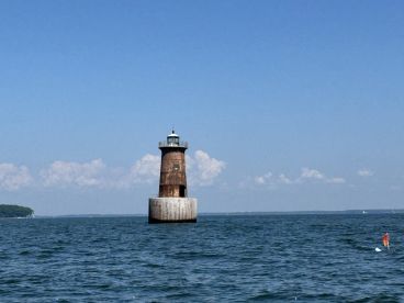 A rustic lighthouse stands prominently in the water, surrounded by a clear blue sky, indicating a serene fishing environment.