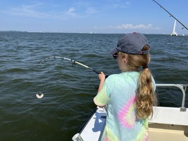 A young angler is reeling in a fish while fishing on a boat, showcasing an exciting moment on the water.