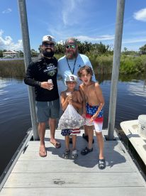 A family group proudly displaying their catch of the day, including a bag of shellfish, while enjoying a sunny day at the dock.