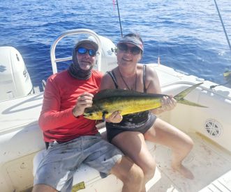 Two anglers proudly displaying a vibrant Mahi Mahi on a fishing boat, showcasing a successful deep-sea fishing trip.