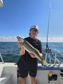 A young angler proudly displaying a Walleye while fishing on a boat, showcasing a beautiful day on the water.