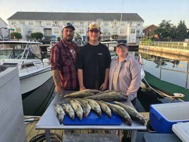 A family poses with their catch of Walleye on a dock after a successful fishing trip, showcasing their haul on a blue cutting board.