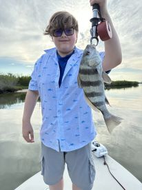 Young angler proudly holding a striped bass while fishing from a boat in a calm waterway.