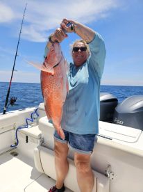 Angler proudly displaying a large Red Snapper while fishing on a boat in open waters.