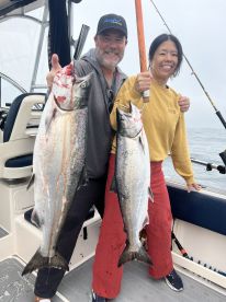 Two anglers proudly displaying their catch of large Salmon while on a fishing trip, showcasing the excitement of a successful day on the water.