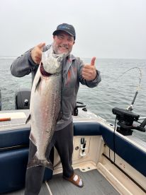 An enthusiastic angler proudly displaying a large Salmon while fishing on a boat in overcast conditions.