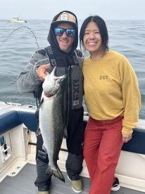 Two anglers proudly displaying a large Salmon on a fishing boat, showcasing a successful day on the water.