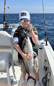 Young angler proudly holding a large fish aboard a boat in open waters, showcasing a successful fishing trip.
