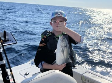 A young angler proudly displaying a caught fish while aboard a boat in open waters.