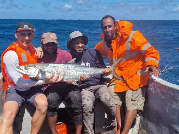 Four anglers proudly displaying a large King Mackerel aboard a fishing boat in open waters.