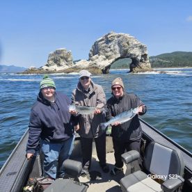 Three anglers proudly displaying their catches of Salmon while enjoying a scenic day on the water, with a striking rock formation in the background.
