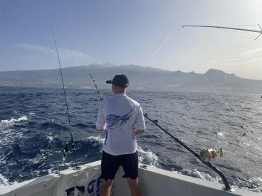 A young angler is actively fishing off the coast, with a scenic backdrop of mountains and a clear sky, showcasing the excitement of deep-sea fishing.