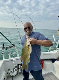 An angler proudly displaying a large Smallmouth Bass while fishing on a boat, with a scenic ocean backdrop.