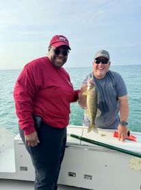 Two anglers proudly displaying a large Walleye while fishing on a boat in clear waters.