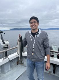 A young angler proudly displaying a freshly caught Salmon aboard a fishing boat in a scenic marine environment.