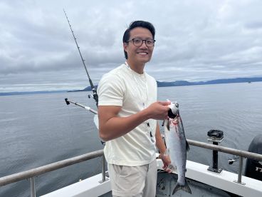 An angler proudly displaying a freshly caught salmon while fishing on a boat in a scenic coastal environment.