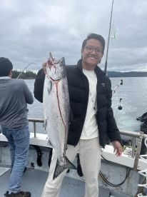 A proud angler displaying a freshly caught Salmon on a fishing charter in a scenic coastal environment.