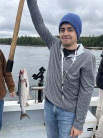 An angler proudly displaying a freshly caught Salmon while fishing on a boat surrounded by lush greenery.