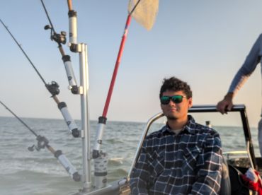 A young angler seated in the helm area of a fishing boat, surrounded by fishing rods, enjoying a day on the water.