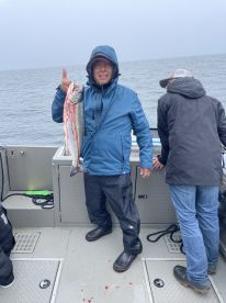 Angler proudly displaying a freshly caught Salmon while fishing on a boat in overcast conditions.