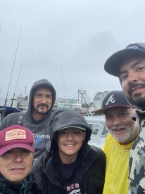 Group of anglers posing together at the dock, dressed for a fishing trip in overcast weather.