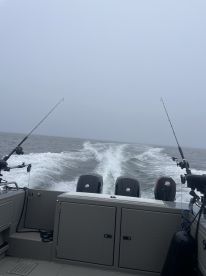 View from the helm of a fishing boat, showcasing the dual engines and fishing rods as it navigates through a foggy sea.