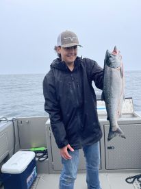 Young angler proudly holding a large salmon while fishing on a boat in open water.