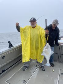 An angler proudly displaying a large Halibut while fishing on a boat in overcast weather.