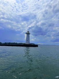 A scenic view of a lighthouse standing tall on the shoreline, surrounded by calm waters and a dramatic sky, ideal for fishing enthusiasts exploring the area.