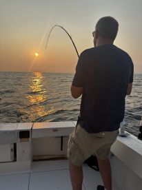 An angler is actively reeling in a fish during a sunset fishing trip, showcasing the excitement of deep-sea fishing.