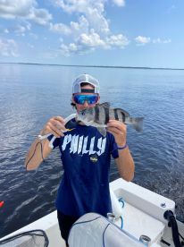 Young angler proudly displaying a striped bass while fishing on a calm day in open water.