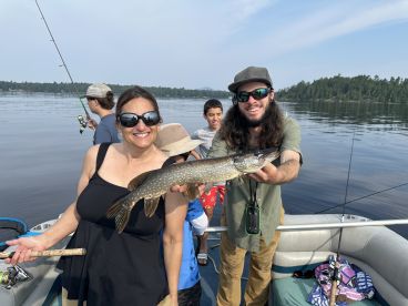 A family enjoying a fishing trip on a lake, with a proud angler displaying a Northern Pike caught from a boat.