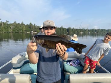 A young angler proudly displaying a large Smallmouth Bass while fishing on a serene lake, surrounded by family.