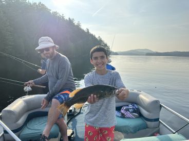A young angler proudly displaying a caught fish while fishing on a serene lake, surrounded by lush greenery.