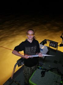 Young angler proudly holding a long fish while night fishing, showcasing the excitement of a successful catch.