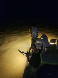 Nighttime fishing action on a boat, with anglers preparing to reel in their catch in murky waters.